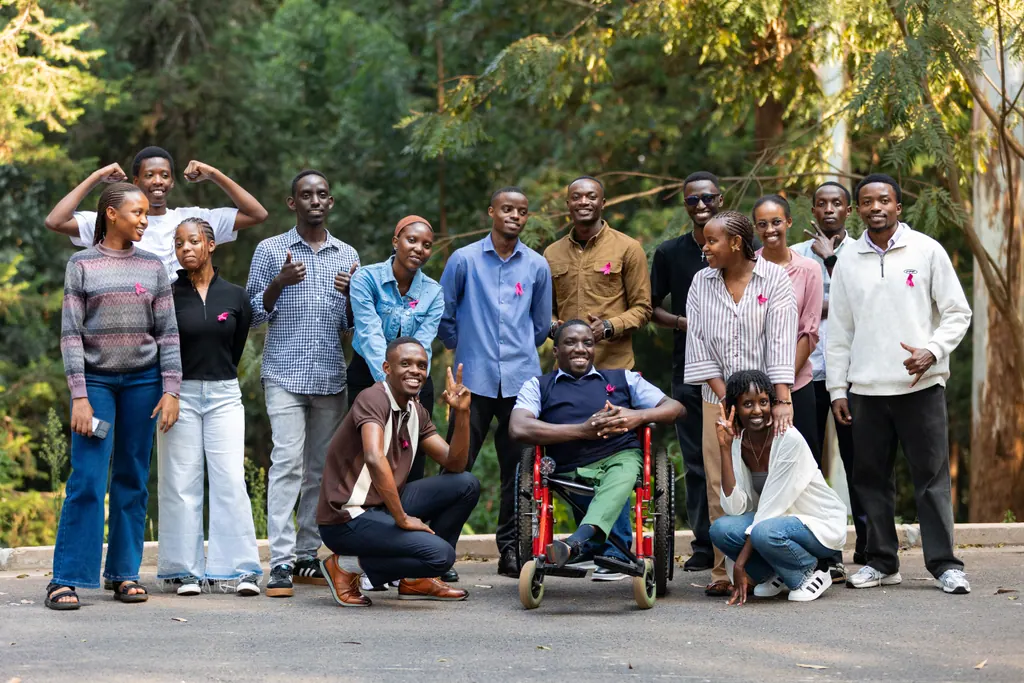 A large group of young people wearing pink ribbons pose together outdoors; one is a wheelchair user.
